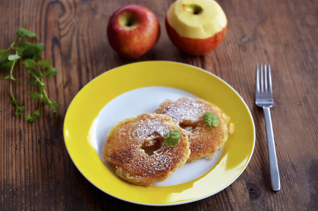 Two battered apple rings with sugar, cinnamon and mint on a yellow plate — Stock Photo