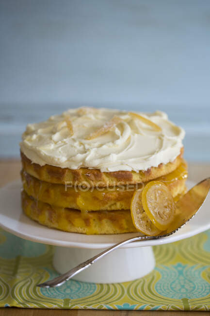 Un pastel de limón de tres capas con glaseado y limones confitados - foto de stock