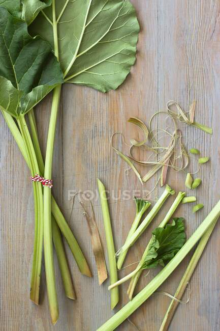 Rhubarbe, partiellement tranchée et entière avec de grandes feuilles sur une table en bois — Photo de stock