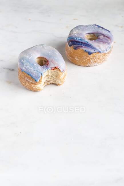 Two galaxy croissant doughnuts with marble glaze, a bite missing — Stock Photo