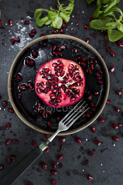 Mezzo melograno e semi di melograno su piatto e superficie nera con forchetta — Foto stock