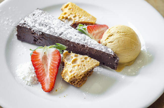 Moist and rich chocolate and honeycomb cake served with honeycomb, ice cream and fresh strawberries decorated with icing sugar — Stock Photo