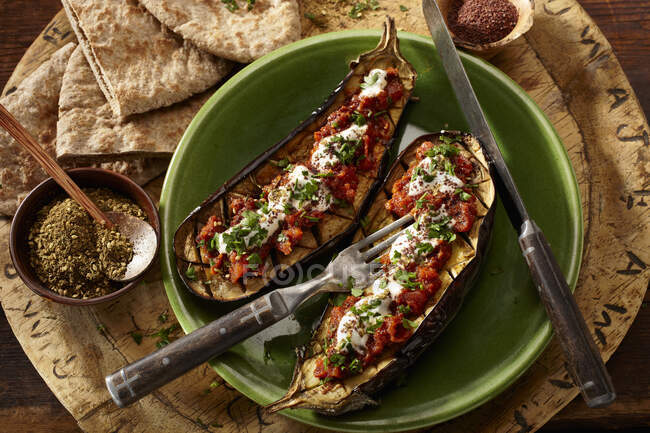 Stuffed and grilled eggplant halves in bowl with cutlery — Stock Photo