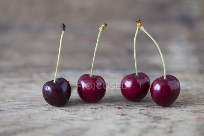 Four fresh cherries on wooden surface, close up — Stock Photo