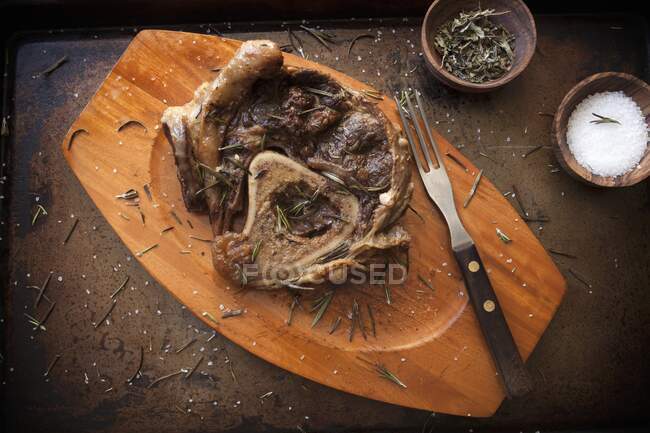 Carne de res estofada con hueso con sal y romero en tabla de cortar madera - foto de stock