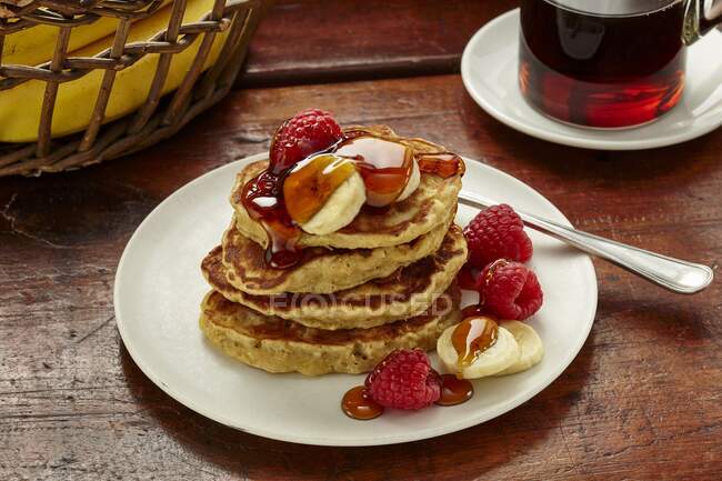 Banana oat pancakes with banana, raspberries and maple syrup — Stock Photo
