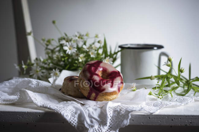 Vegan doughnuts with two types of glaze on an old wooden chair with coffee and flowers — Stock Photo