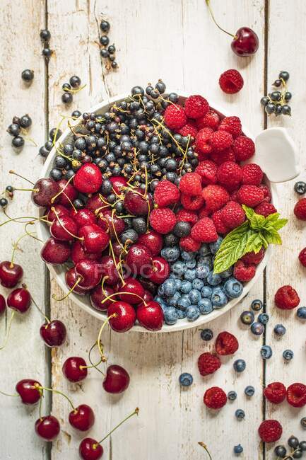 Cherries, blueberries, blackcurrants and raspberries in bowl and on wooden table — Stock Photo