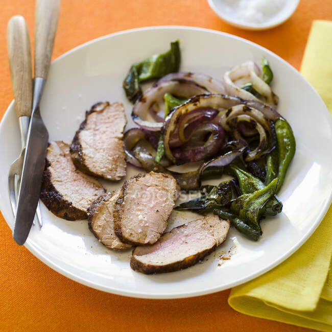 Sliced pork tenderloin with onions and greens — Stock Photo