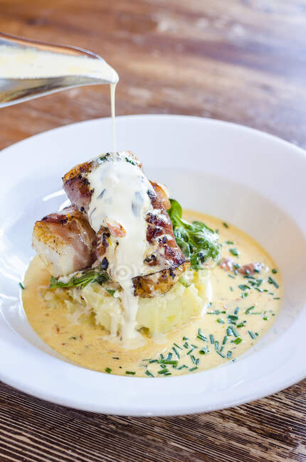 Sea bass fish fillets wrapped in bacon on a potato mash with spinach and chives with a pour of white wine sauce — Stock Photo
