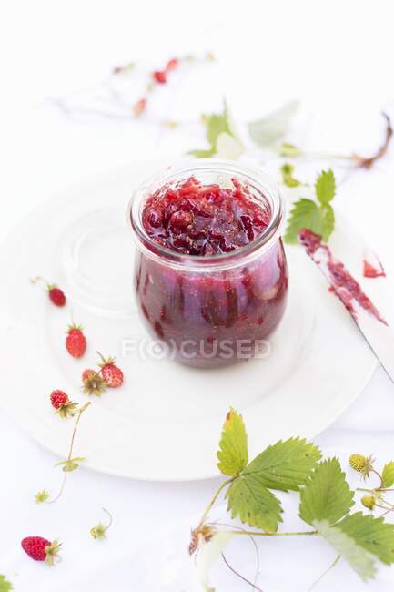Mermelada de fresas silvestres caseras en frasco de vidrio con bayas frescas y hojas en el plato - foto de stock