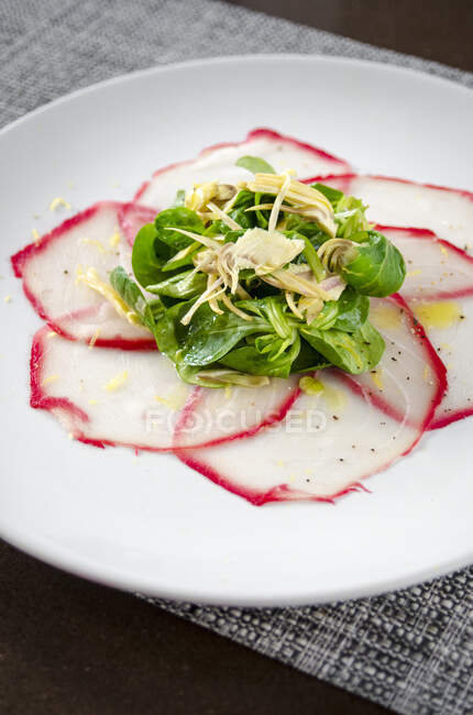 Fresh tuna carpaccio with herb salad and artichokes drizzled with olive oil on a white plate — Stock Photo