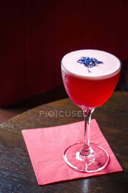 Red cocktail decorated with cornflowers on a red napkin and wooden table — Stock Photo