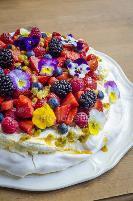 Pavlova with whipped cream, berries, passion fruit and edible flowers — Stock Photo