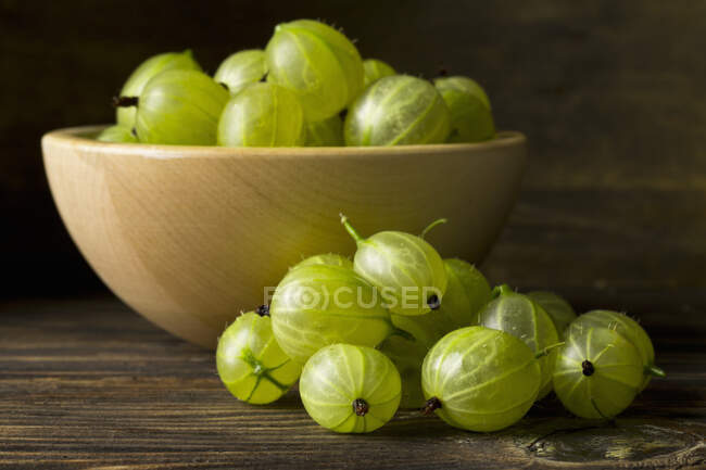Uva spina verde in ciotola di legno e sulla superficie del tavolo — Foto stock