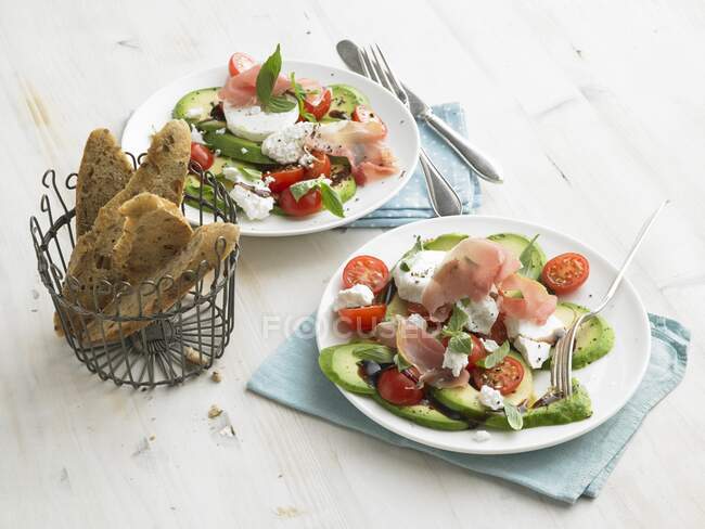 Avocado with goat's cheese, raw ham, cherry tomatoes and wholegrain baguette slices — Stock Photo