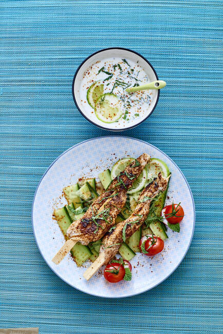 Chicken skewers on cucumber strips with yoghurt sauce — Stock Photo