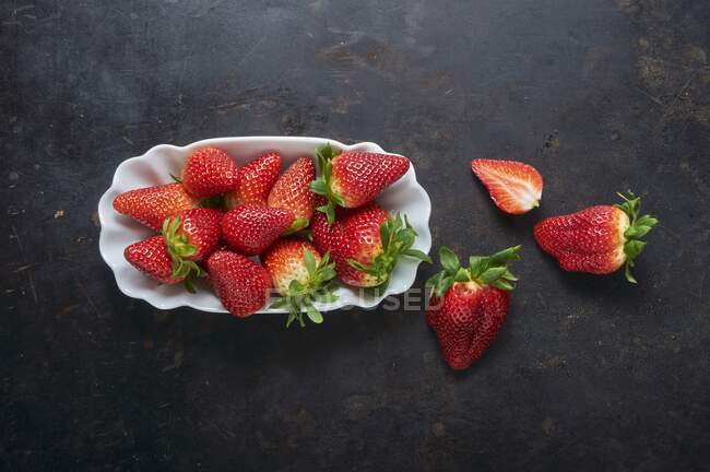 Fresh strawberries in white ceramic dish on black metal surface — Stock Photo