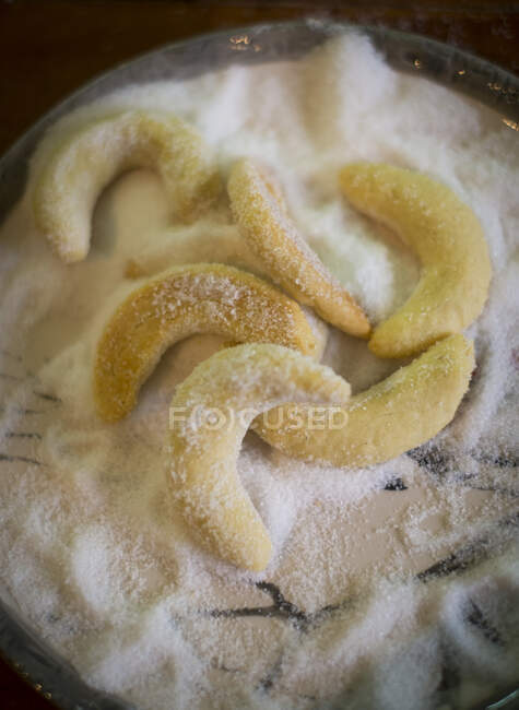 Biscuits croissants à la vanille cuits au four en cours de roulage dans le sucre — Photo de stock