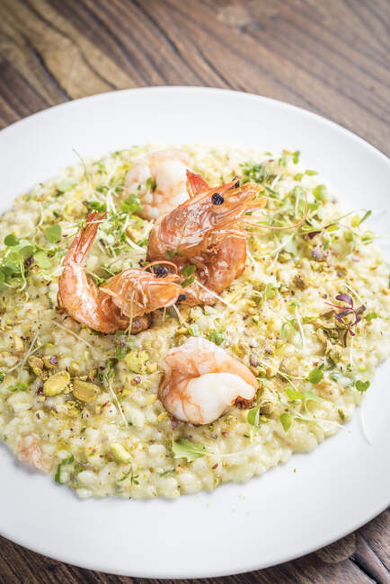 Sicilian pistachio and king prawns risotto with herbs on a white plate and a wooden background — Stock Photo