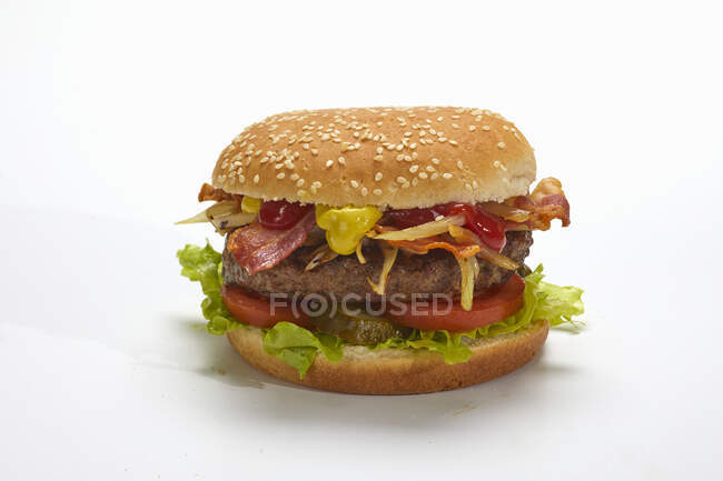Una hamburguesa con tocino y queso contra una superficie blanca - foto de stock