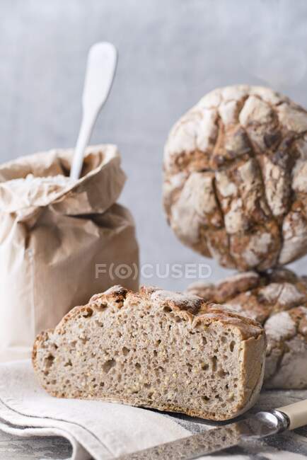 Homemade sourdough bread on a cloth next to a bag of flour and a knife — Stock Photo