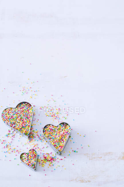 Набір з трьох серцевих печива, наповнених барвистими посипаними на білій поверхні — стокове фото