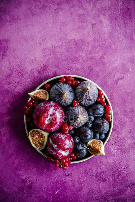 Prunes, figues et groseilles rouges en assiette sur surface rose — Photo de stock
