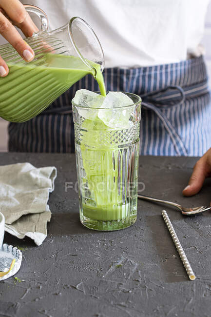 Woman pours matcha tea into a glass with ice cubes — Stock Photo
