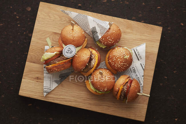 Mini hamburgers on sticks with newspaper pieces on wooden board — Stock Photo