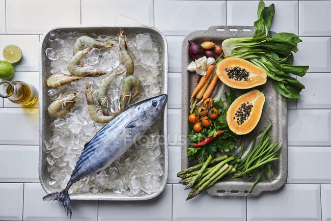Bonito und Tigergarnelen auf Eis, mit Gemüse und Papaya auf Backblechen — Stockfoto