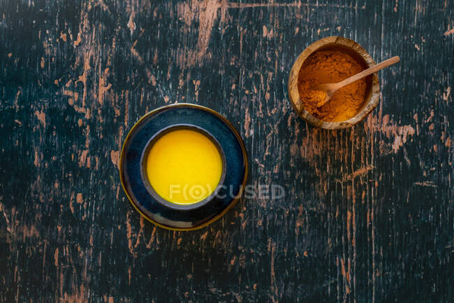 Leche dorada de cúrcuma en platillo y superficie de madera verde angustiada - foto de stock