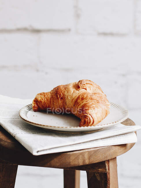 Petit déjeuner croissant et journal sur un tabouret en bois — Photo de stock