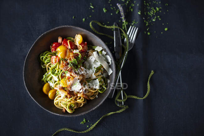 Yellow and green spaghetti with a colorful tomato and bacon sauce — Stock Photo