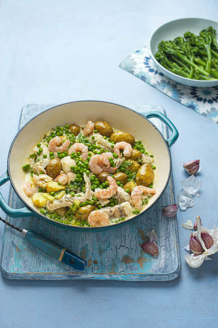 Una pentola di pesce e gamberi con patate novelle e salsa all'aglio cremosa con piselli freschi e broccoli — Foto stock