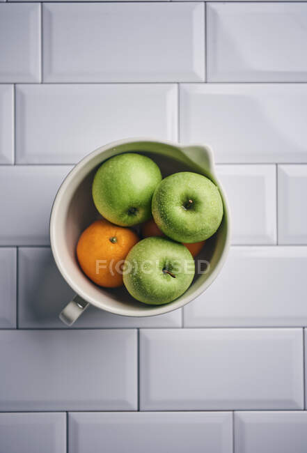 Maçãs verdes e laranjas em uma tigela de cerâmica — Fotografia de Stock