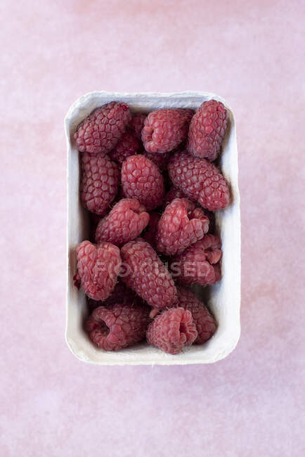 Fresh raspberries in paper box on pink surface — Stock Photo