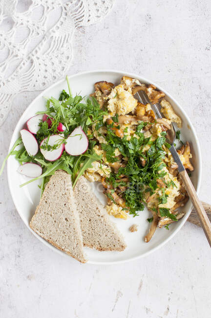 Scrambled eggs with wild mushrooms served with vegetables and slice of bread — Stock Photo