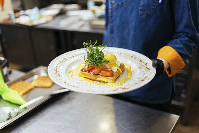 Chef holding plate of waffle with poached egg, salmon and mustard sauce — Stock Photo