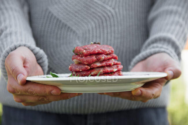 Man is holding burger patties for BBQ — Stock Photo