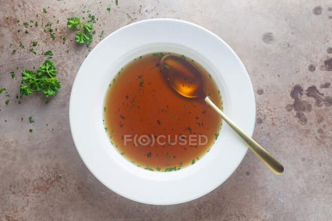Clear beef broth with herbs on metal surface — Stock Photo