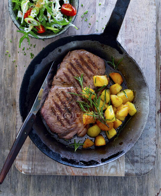 Rump steak with rosemary potatoes in a pan — Stock Photo