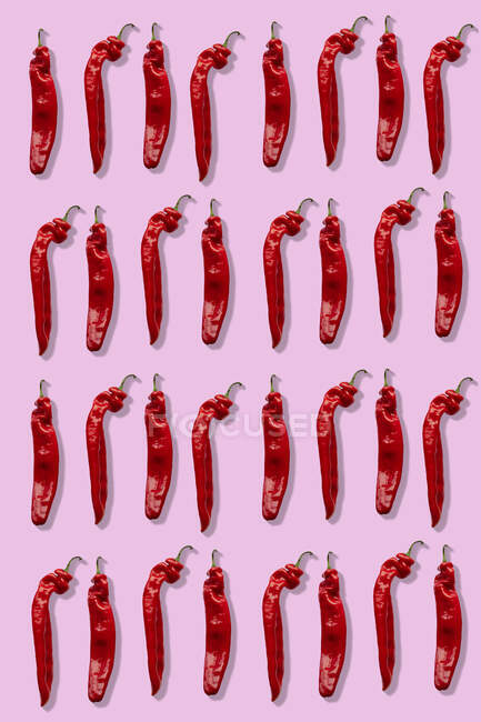 Cuatro filas de chiles rojos sobre un fondo rosa - foto de stock