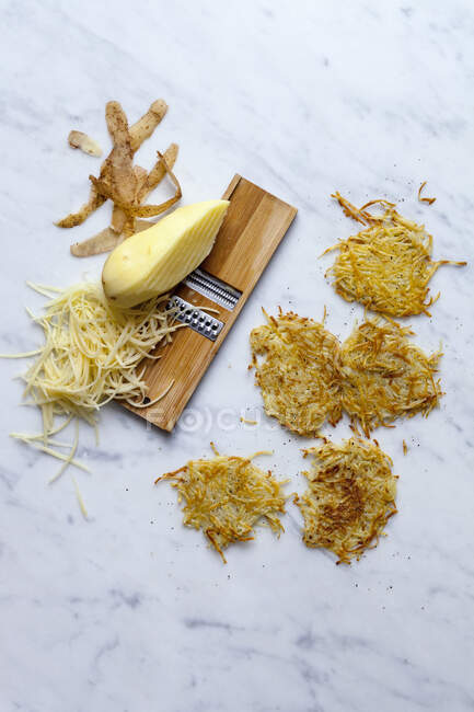 Rosti and raw potatoes on a vegetable grater — Stock Photo
