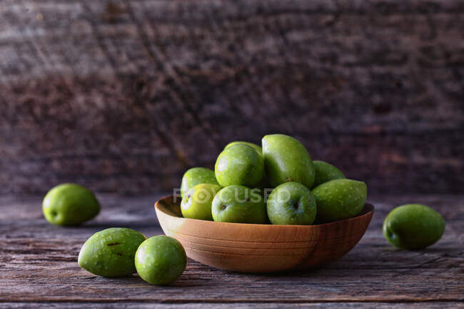 Green olives in a bowl on a wooden background — Stock Photo