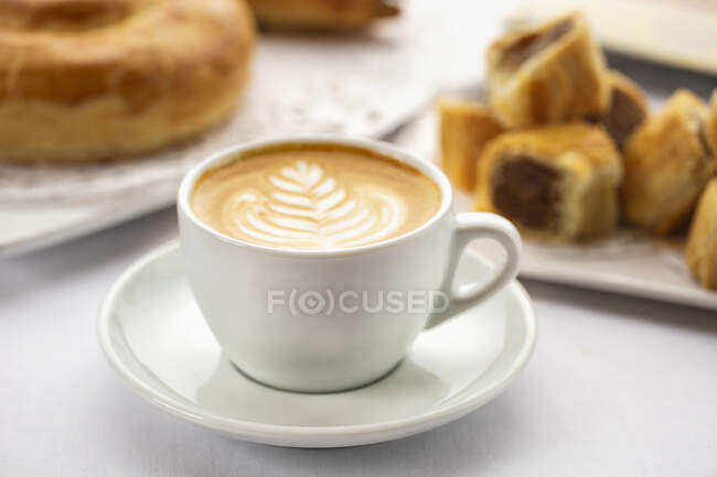 Café avec un motif artistique en mousse de lait et pâtisseries sucrées — Photo de stock