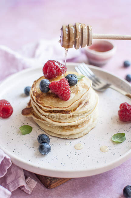 Pancakes with honey and blueberries and raspberries — Stock Photo