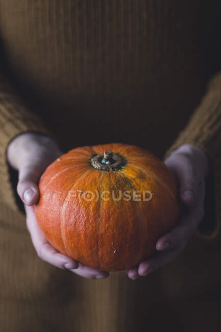 Hands holding a pumpkin with a large white pattern on a wooden background. — Stock Photo
