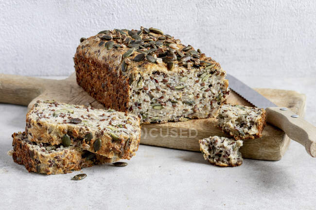 Oat bread with slices on wooden board with knife — Stock Photo
