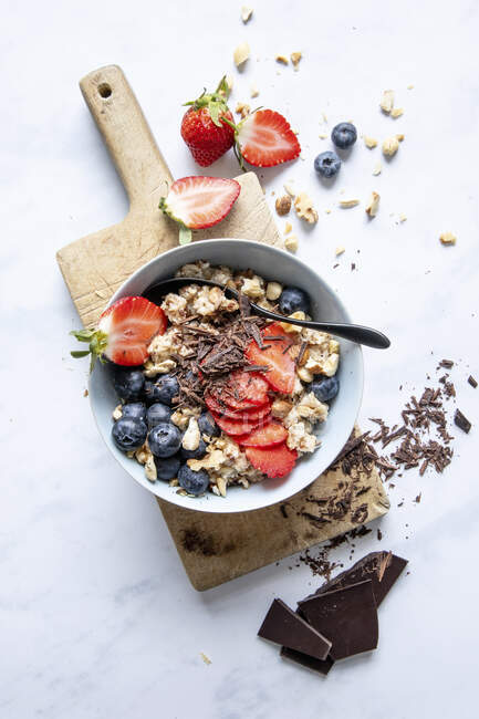 Bowl of porridge with strawberries, blueberries and chocolate shavings — Stock Photo